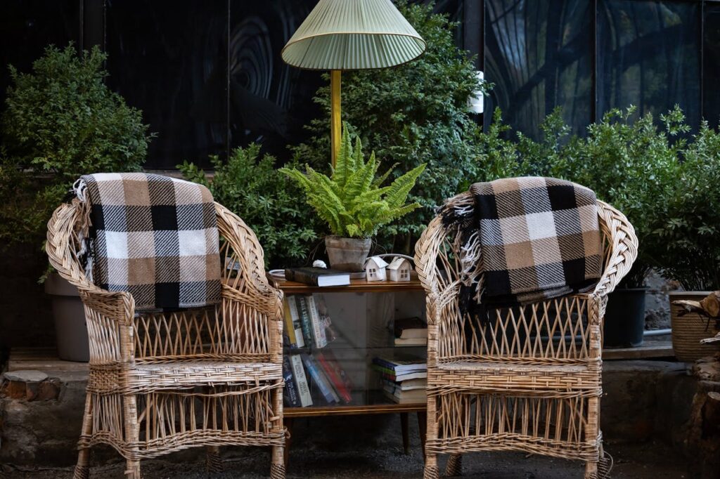 A serene setup with wicker chairs, checkered blankets, and lush fern in natural light.