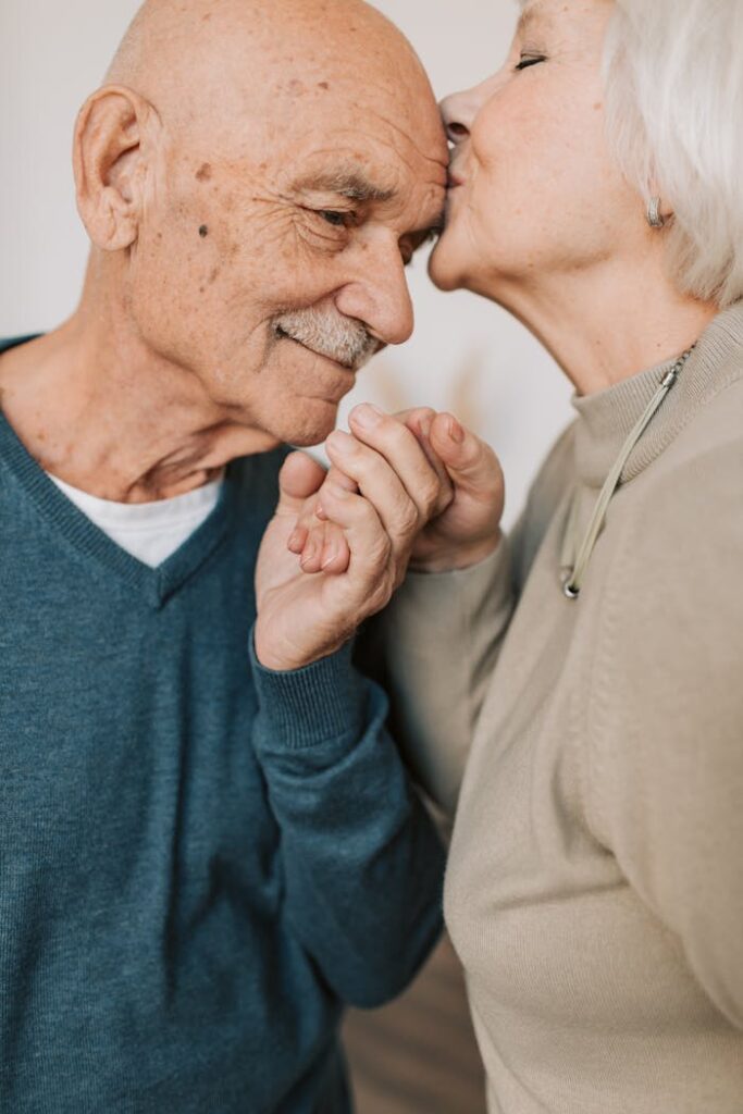 Elderly couple sharing a tender moment with a loving kiss and holding hands.