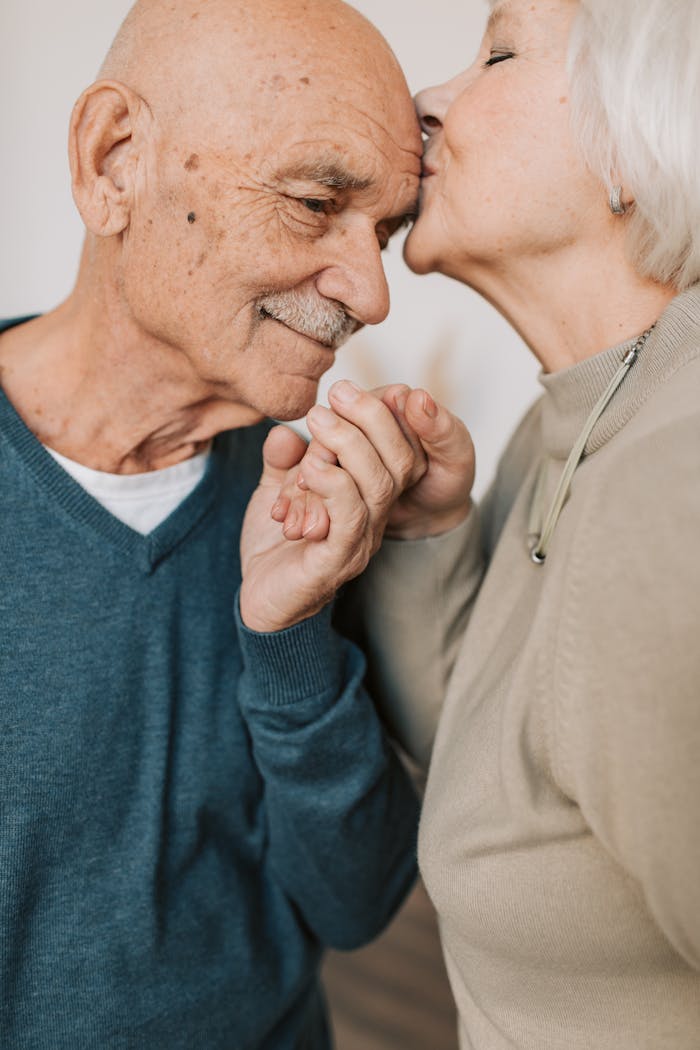 Elderly couple sharing a tender moment with a loving kiss and holding hands.